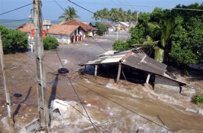 Tidal waves wash through houses at Maddampegama, about 60 kilometers (38 miles) south of Colombo, Sri Lanka, Sunday, Dec. 26, 2004. Massive waves triggered by earthquakes crashed into villages along a wide stretch of Sri Lankan coastline on Sunday, killing more than 2,100 people and displacing a million others. [AP]