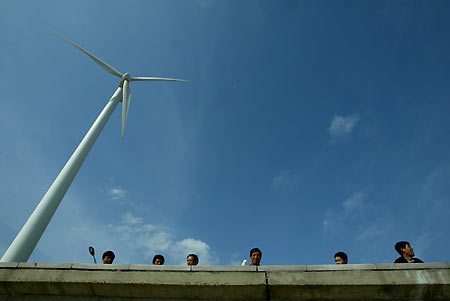 Chinese people stand behind the wall of a windmills site, used as an energy source, at Feng Xian in Shanghai, China February 24, 2006. China, faced with a growing shortage of energy as the economy gallops forward, is looking to add energy conservation as a criterion of officials' performance reviews, a planning official said on Thursday.